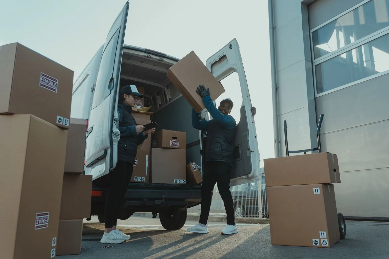Two delivery workers loading cardboard parcels into a white cargo van.
