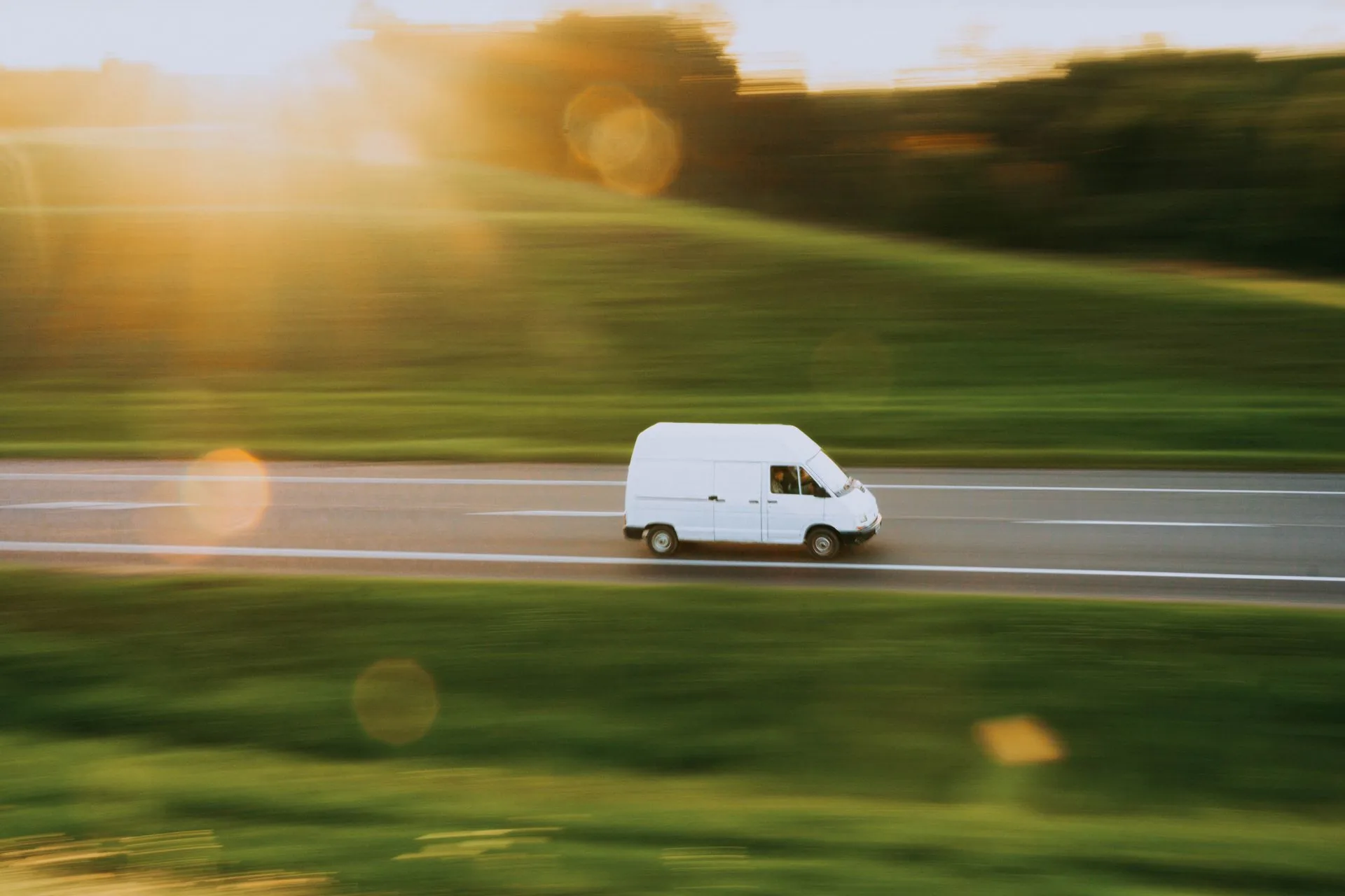 A white cargo van traveling along a country road at sunset.